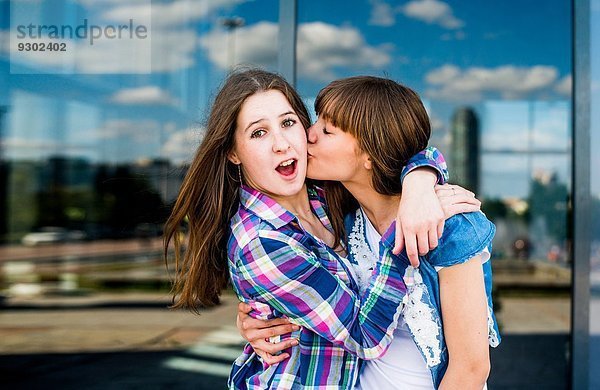 Zwei junge Frauen  die sich mit einem Kuss auf die Wange umarmen.