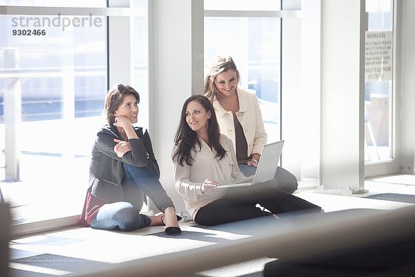 Drei Geschäftsfrauen sitzen auf dem Boden mit Laptop im Konferenzzentrum