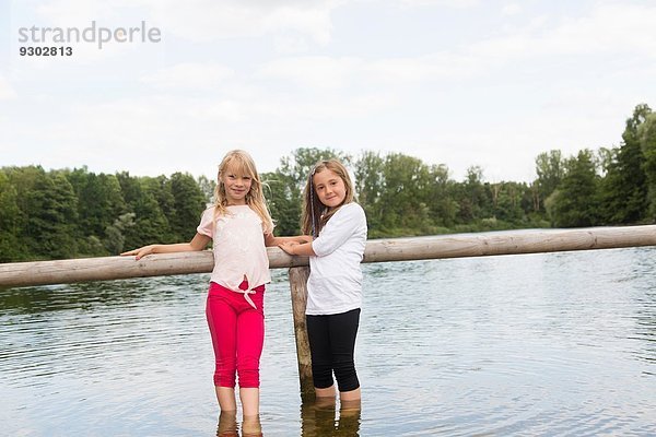 Porträt von zwei Mädchen  die sich am Zaun festhalten  während sie im See paddeln.