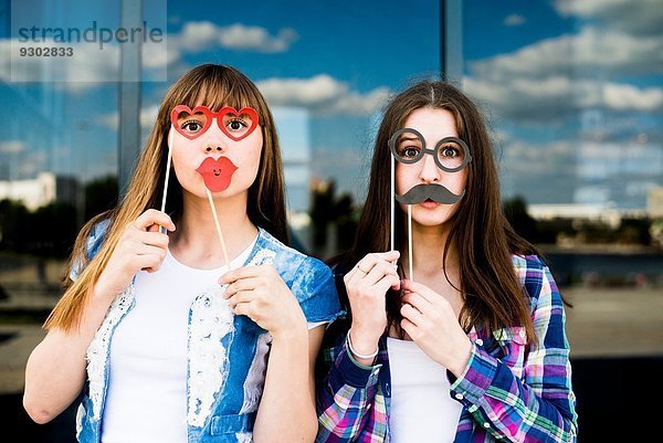 Porträt von zwei jungen Frauen  die Lippen- und Augenmasken hochhalten.