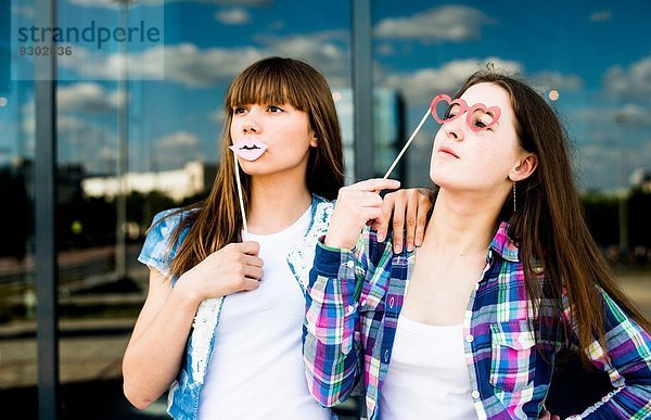 Zwei junge Frauen  die mit Lippen- und Brillenmasken aufblicken.