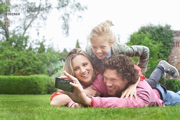 Vater fotografiert Familie auf dem Rasen liegend