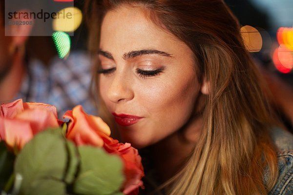 Junge Frau mit Freund riecht Rosen im Stadttaxi bei Nacht