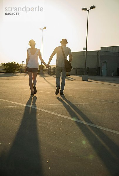 Romantisches junges Paar schlendert Hand in Hand über den leeren Parkplatz