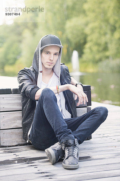 Junger Mann mit Lederjacke sitzt in einem Park