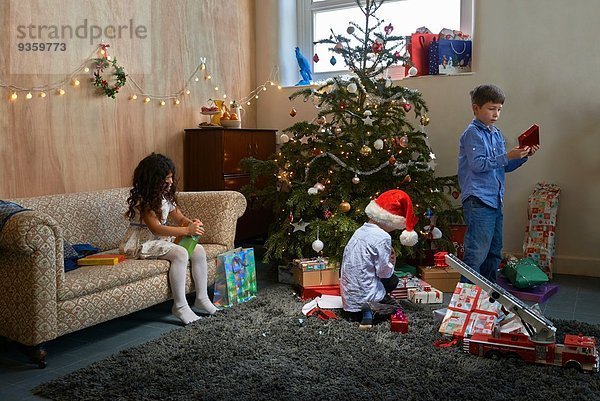 Mädchen und zwei Brüder eröffnen Weihnachtsgeschenke im Wohnzimmer