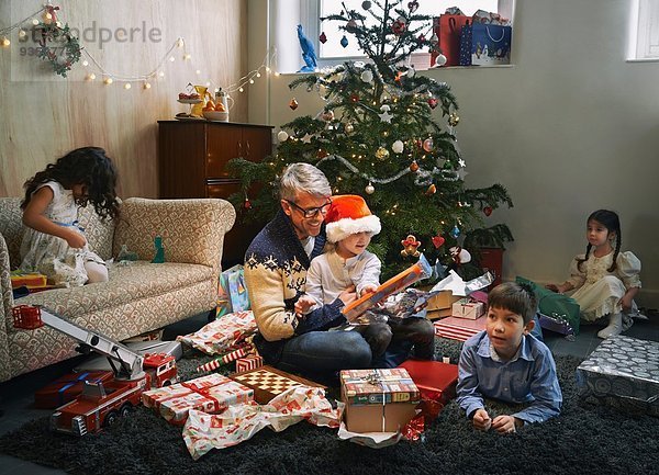 Vater und vier Kinder eröffnen Weihnachtsgeschenke im Wohnzimmer