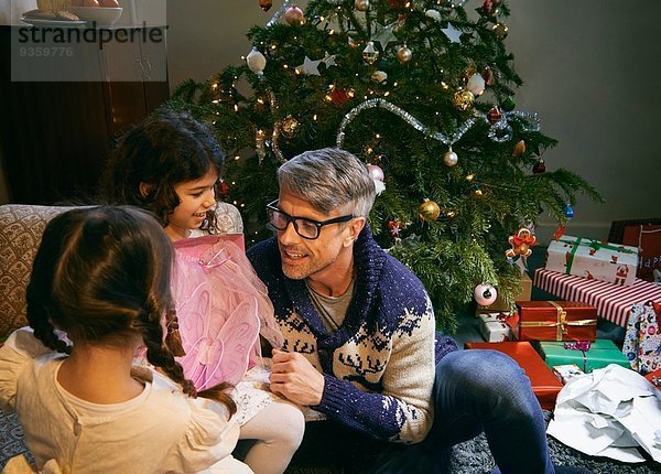 Vater und zwei Töchter eröffnen Weihnachtsgeschenke im Wohnzimmer