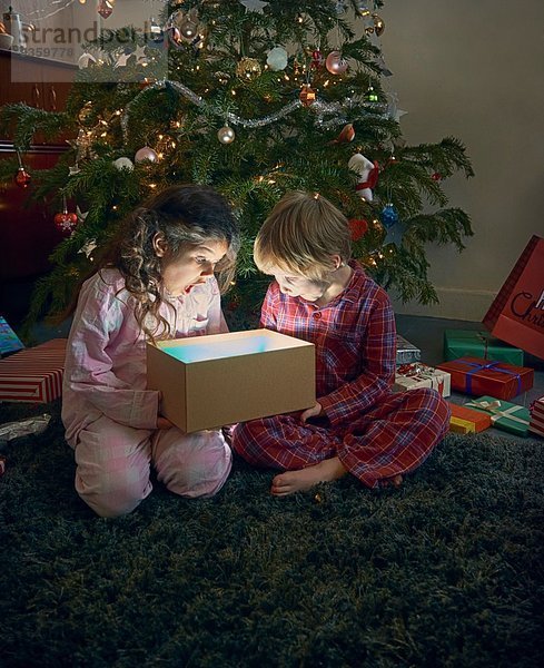 Schwester und Bruder öffnen den Mund und packen die glühende Weihnachtsgeschenkbox aus.