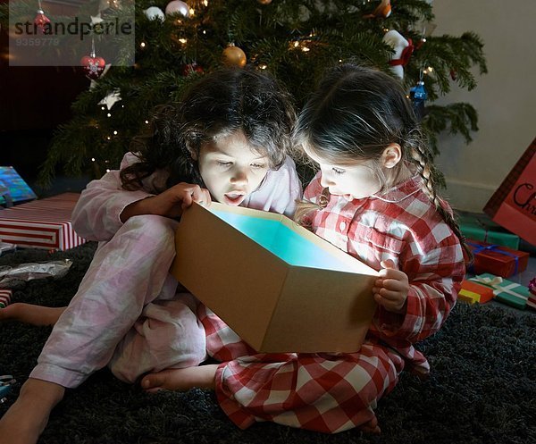 Zwei Schwestern öffnen den Mund und packen die glühende Weihnachtsgeschenkbox aus.