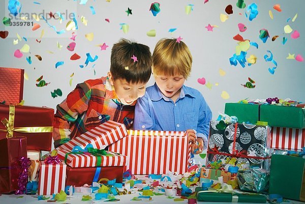 Zwei Brüder öffnen Mund auf Auspacken glühenden Weihnachtsgeschenkbox mit explodierenden Konfetti