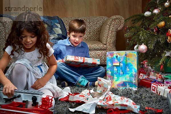 Schwester und Bruder im Wohnzimmer beim Auspacken und Spielen mit Weihnachtsgeschenken