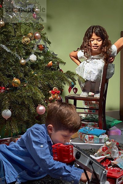 Schwester beobachtet Bruder beim Auspacken und Spielen mit Weihnachtsgeschenken