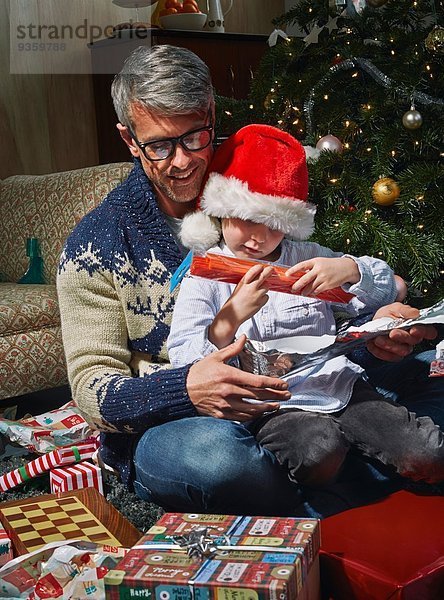 Vater auf dem Wohnzimmerboden öffnet Weihnachtsgeschenke mit Sohn