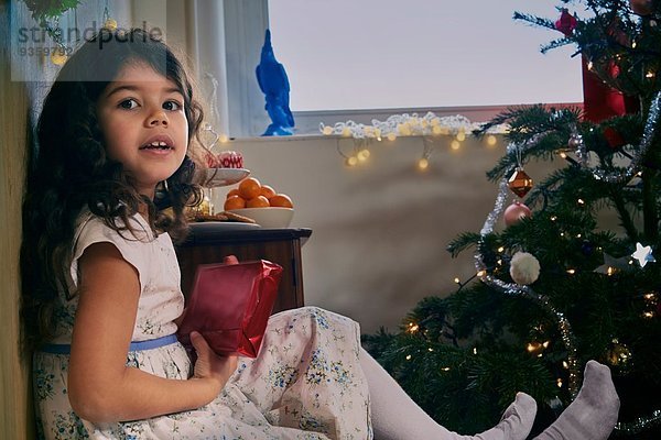 Porträt eines auf dem Boden sitzenden Mädchens mit Weihnachtsgeschenk