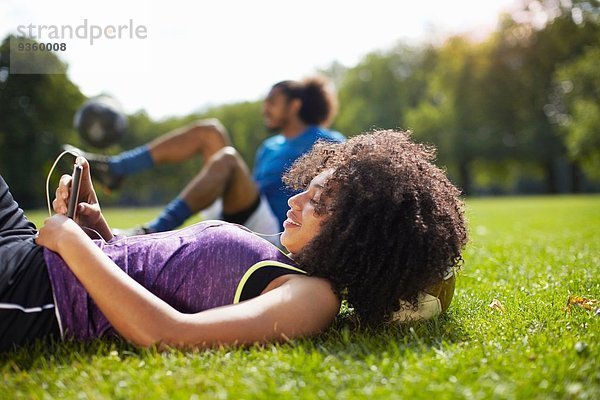 Junge Frau macht Pause beim Lesen von Texten auf dem Smartphone im Park