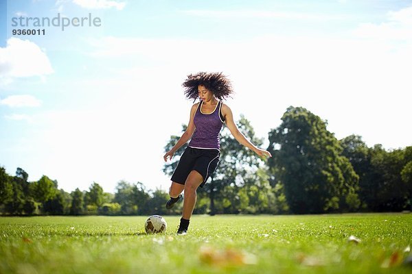 Junge Frau tritt Fußball im Park