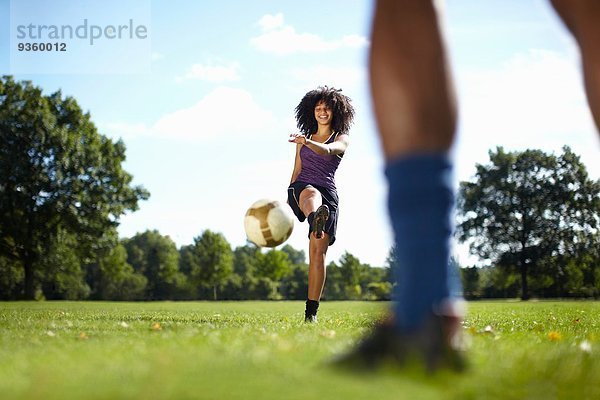 Junge Frau tritt Fußball in Richtung Freund im Park