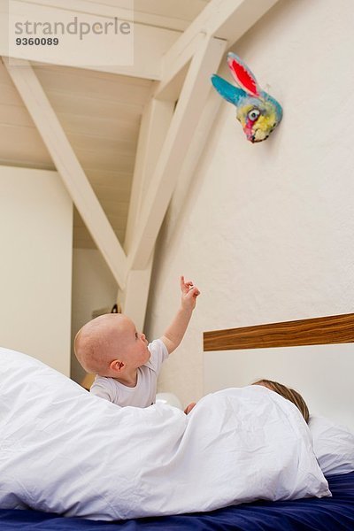 Kleines Mädchen  das aus dem Bett zeigt  während die Mutter unter der Decke liegt.