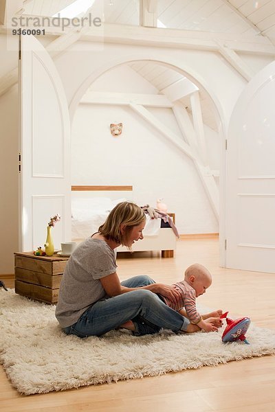 Reife Mutter und kleine Tochter beim Spielen auf dem Teppich im Wohnzimmer