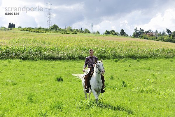 Junger Mann mit Cowboyhut im Galopp auf dem Feld