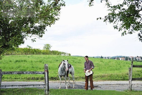 Junger Mann in Cowboy-Ausrüstung führt Pferd durchs Tor