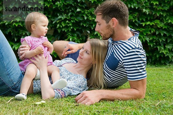 Mittleres erwachsenes Paar mit kleiner Tochter auf Rasen im Garten liegend