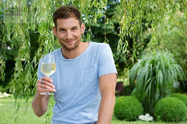 Porträt eines erwachsenen Mannes mit einem Glas Weißwein im Garten