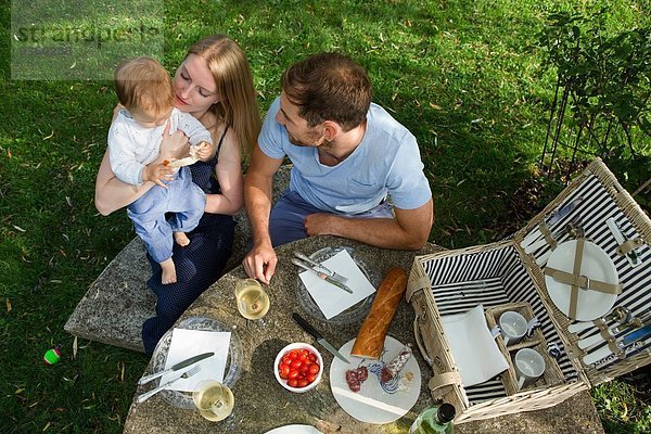Ansicht des mittleren erwachsenen Paares und der kleinen Tochter am Picknicktisch im Garten
