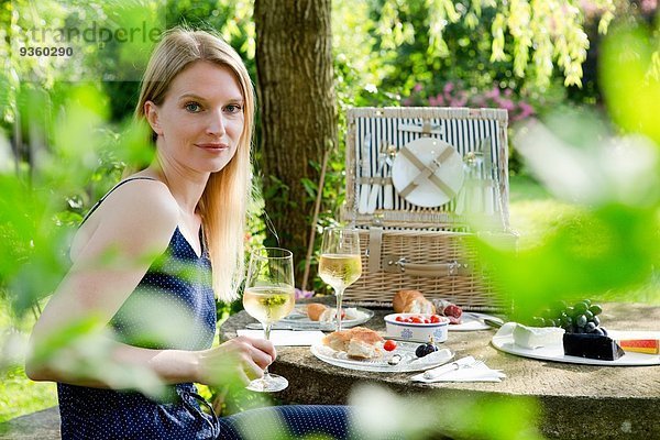 Porträt einer mittleren erwachsenen Frau am Picknicktisch mit einem Glas Weißwein im Garten