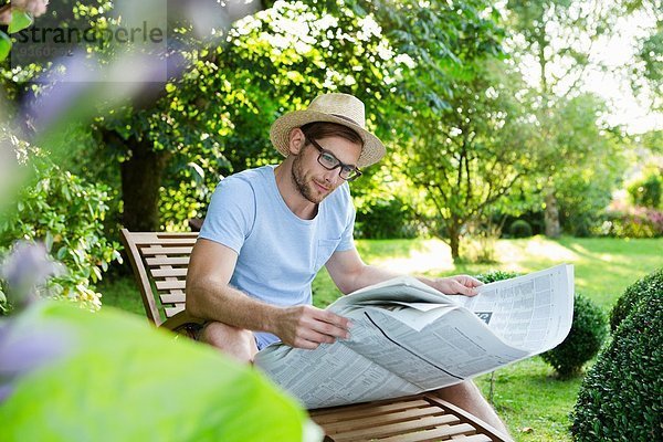 Mittlerer Erwachsener Mann beim Zeitungslesen im Garten