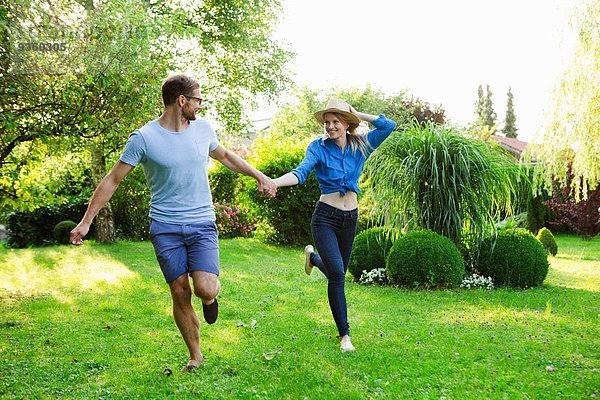 Mittleres erwachsenes Paar hält sich beim Laufen im Garten an den Händen