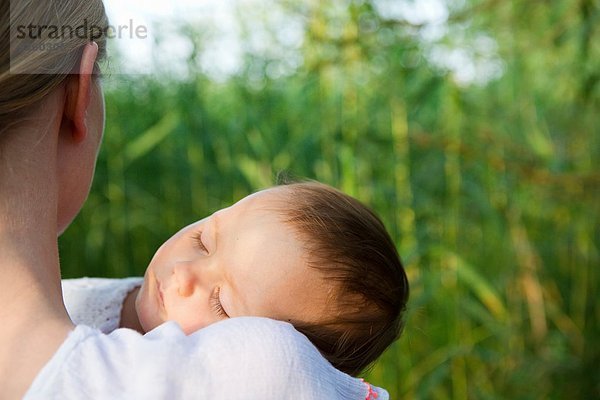 Über-Schulter-Porträt der mittleren erwachsenen Mutter und schlafenden Tochter im Garten