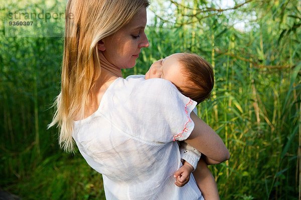 Rückansicht der mittleren erwachsenen Mutter und schlafenden Tochter im Garten