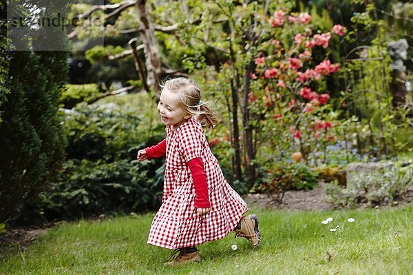 Junges Mädchen im Gingham-Kleid  das im Garten läuft