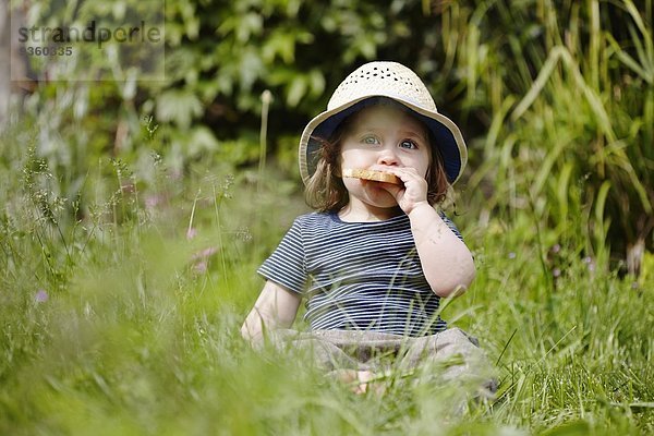 Junges Mädchen sitzt im Gras und isst einen Snack.