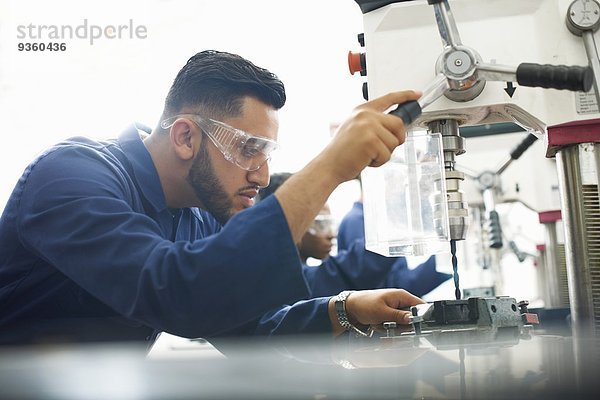 Männlicher Student mit Bohrmaschine in der College-Werkstatt