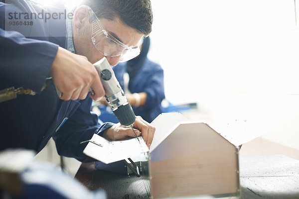 Männlicher Student mit Handbohrmaschine in der College-Werkstatt