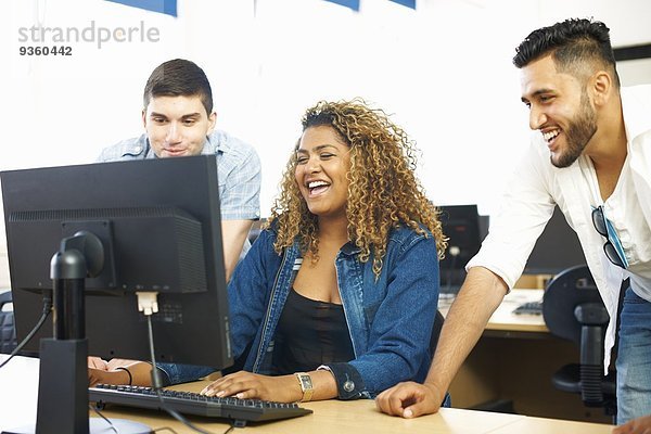 Drei Studentenfreunde beim Lachen und Anschauen des PCs im Klassenzimmer