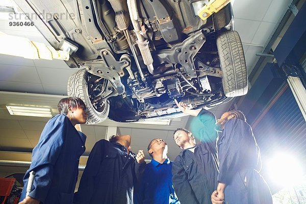 Fünf Studenten schauen in der Werkstatt unter dem Auto nach oben