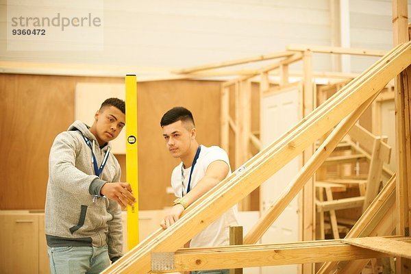 Zwei männliche Studenten mit Wasserwaage in der Holzbearbeitungswerkstatt