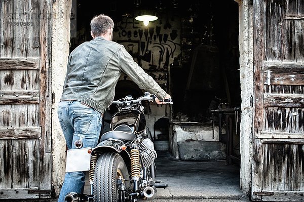 Mittlerer Erwachsener Mann schiebt Motorrad in die Scheune