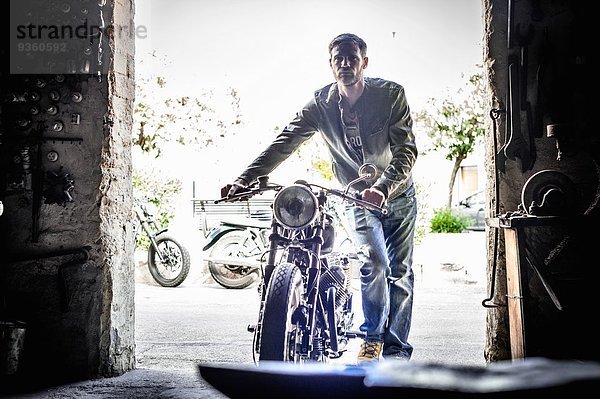 Mittlerer Erwachsener Mann schiebt Motorrad durch die Scheunentür