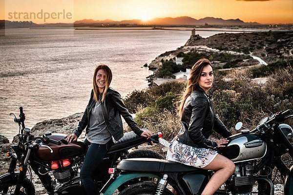 Portrait von zwei Motorradfahrerinnen an der Küste bei Sonnenuntergang  Cagliari  Sardinien  Italien