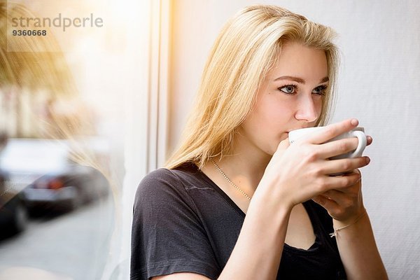 Junge Frau trinkt Kaffee im Fenstersitz