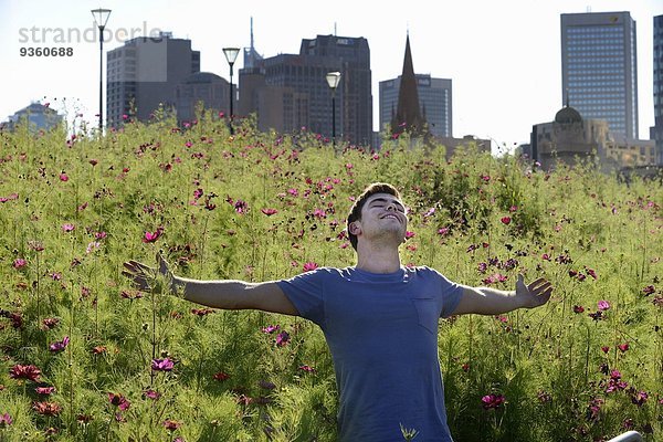 Junger Mann  Arme ausgestreckt  gegen Wildblumen und Stadtbild