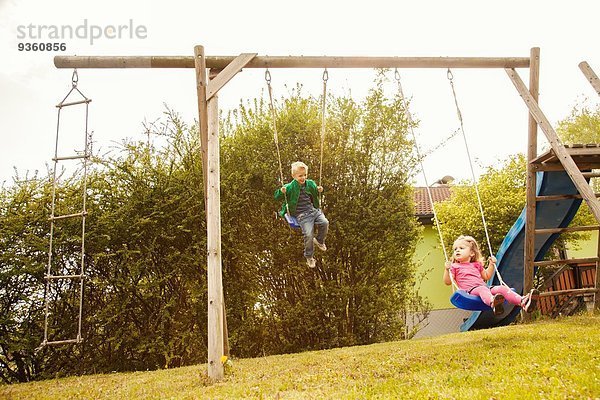 Geschwister spielen auf Schaukeln im Garten