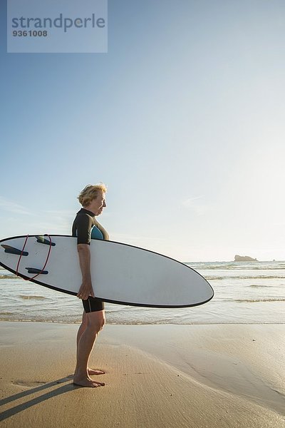 Seniorin am Strand stehend mit Surfbrett  Camaret-sur-mer  Bretagne  Frankreich