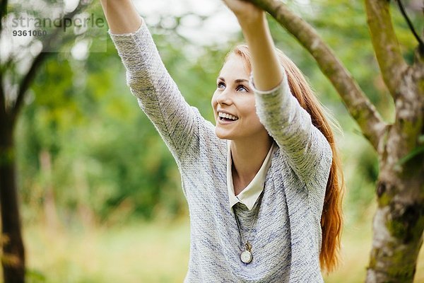 Junge Frau im Feld  die sich an einem Baumzweig festhält