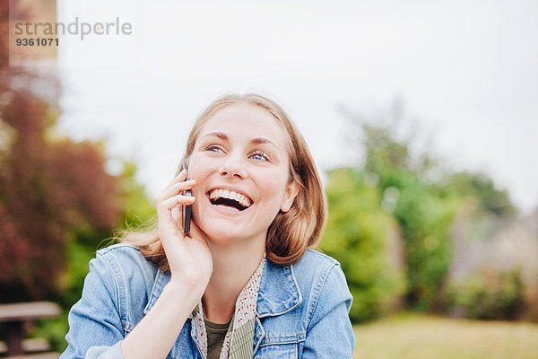 Junge Frau lacht beim Chatten auf dem Smartphone im Park
